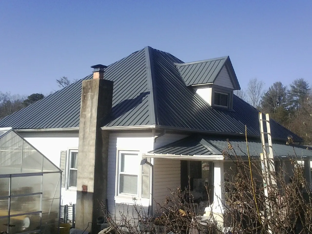 Dark blue standing seam metal roof on a white farmhouse with dormer — Slate & Tile Roof Repair by Roofing Brothers in Evergreen