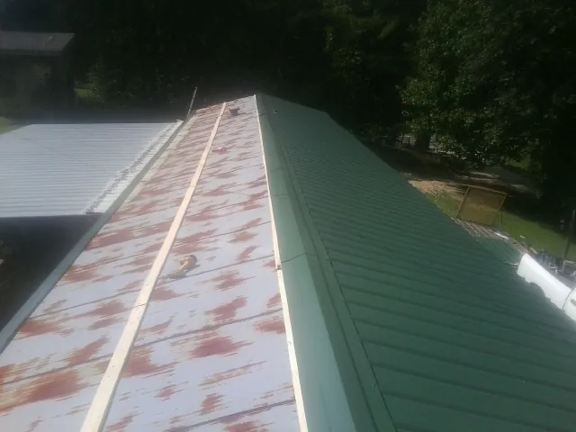 Old rusted panels beside newly installed green metal roofing — Wind Damage Roof Repair by Roofing Brothers in Evergreen