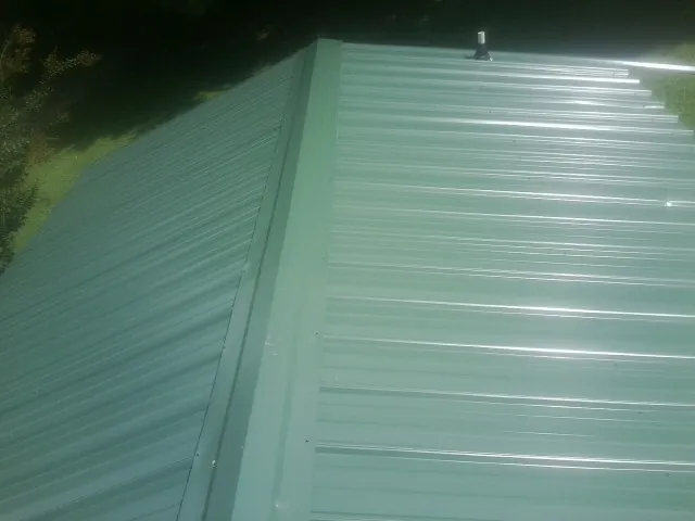 New green metal panels meeting at the ridge of a roof — Flat Roof Repair work by our crew in Evergreen