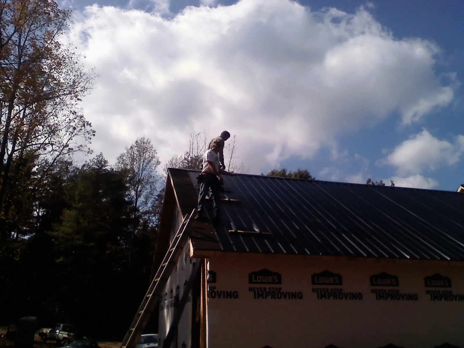 Roofer fastening dark metal panels high against a cloudy sky, from a Roof Inspection job in Evergreen