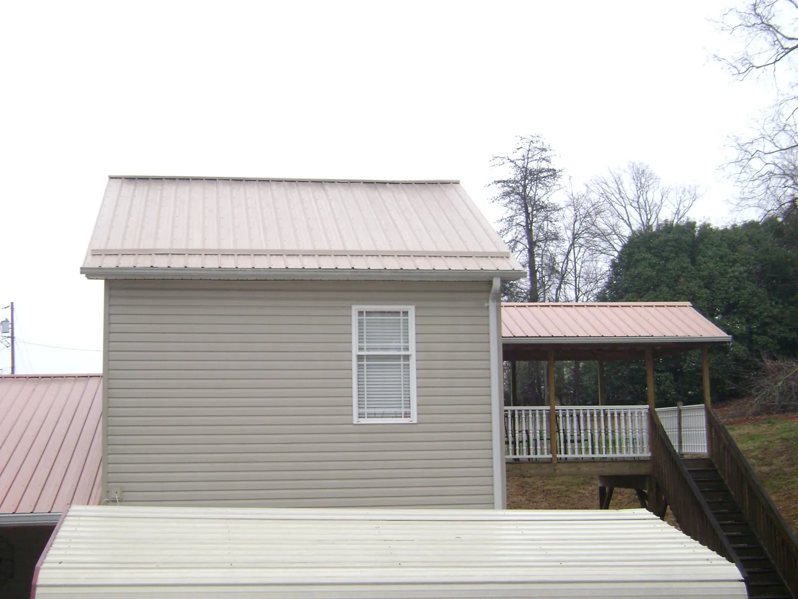 Tan metal roofs on a two story addition and attached porch, from a Roof Replacement job in Evergreen